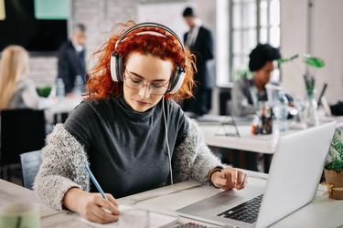 Rothaarige Studierende vor dem Laptop schreibt auf einem Block. 