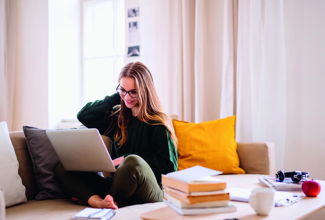 Lernende zuhause mit Laptop und Büchern auf der Couch